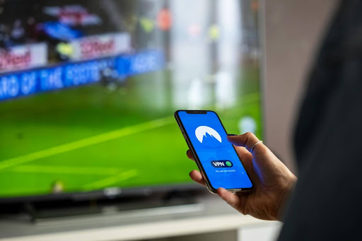 hand-holding-phone-with-football-game-on-background-tv